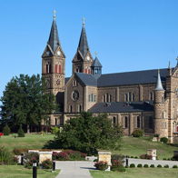 Grand cathedral with tall spires, surrounded by greenery, set against a bright sky, evoking tranquility and reverence.