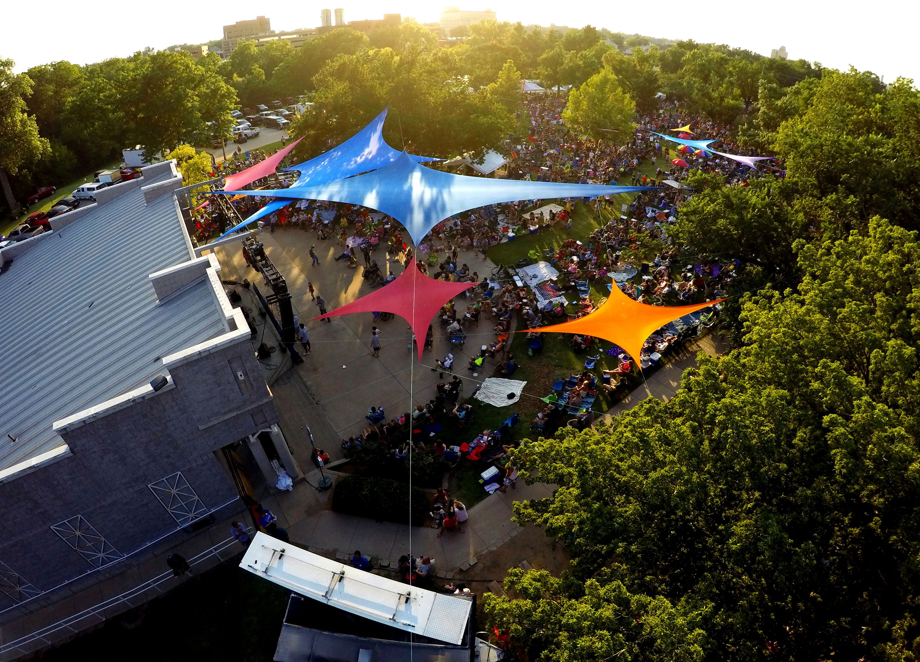 Vibrant outdoor festival with colorful canopies, a large crowd, and lush trees creating a joyful and lively community atmosphere.