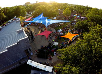Vibrant outdoor festival with colorful canopies, a large crowd, and lush trees creating a joyful and lively community atmosphere.