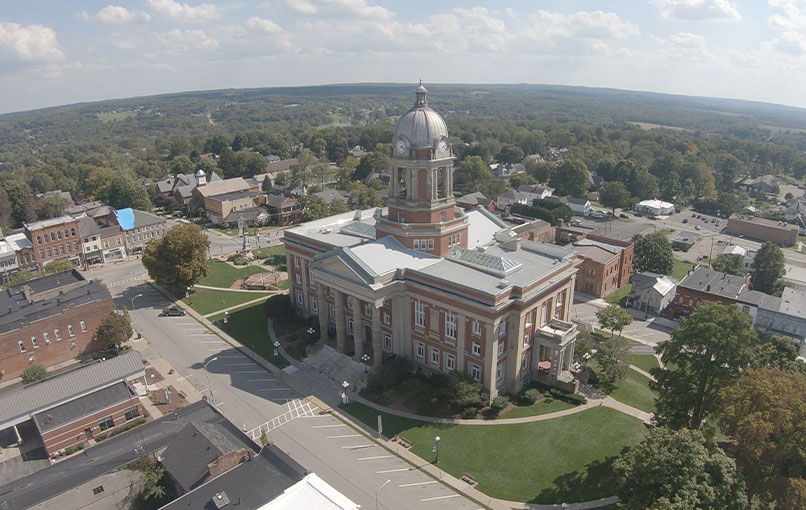 Aerial view of a town with a classic courthouse, surrounded by lawns and hills, evoking tranquility and community pride.