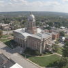 Aerial view of a town with a classic courthouse, surrounded by lawns and hills, evoking tranquility and community pride.