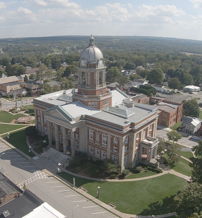Aerial view of a town with a classic courthouse, surrounded by lawns and hills, evoking tranquility and community pride.