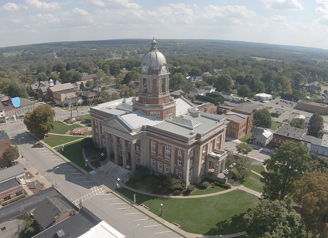 Aerial view of a town with a classic courthouse, surrounded by lawns and hills, evoking tranquility and community pride.