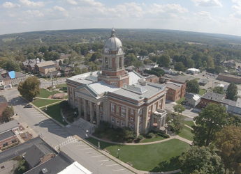 Aerial view of a town with a classic courthouse, surrounded by lawns and hills, evoking tranquility and community pride.