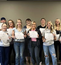 Group of individuals holding certificates, expressing joy and pride, celebrating achievement in a neutral backdrop.