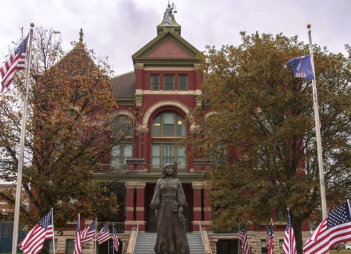 Red brick building with historical architecture, statue of a woman, American flags, and autumn foliage create a patriotic scene.