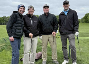 Four friends in golf attire smile on a course, exuding camaraderie and joy amidst a cloudy outdoor setting.