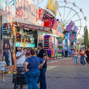 A vibrant carnival scene with colorful booths, a Ferris wheel, and joyful people enjoying festivities together.