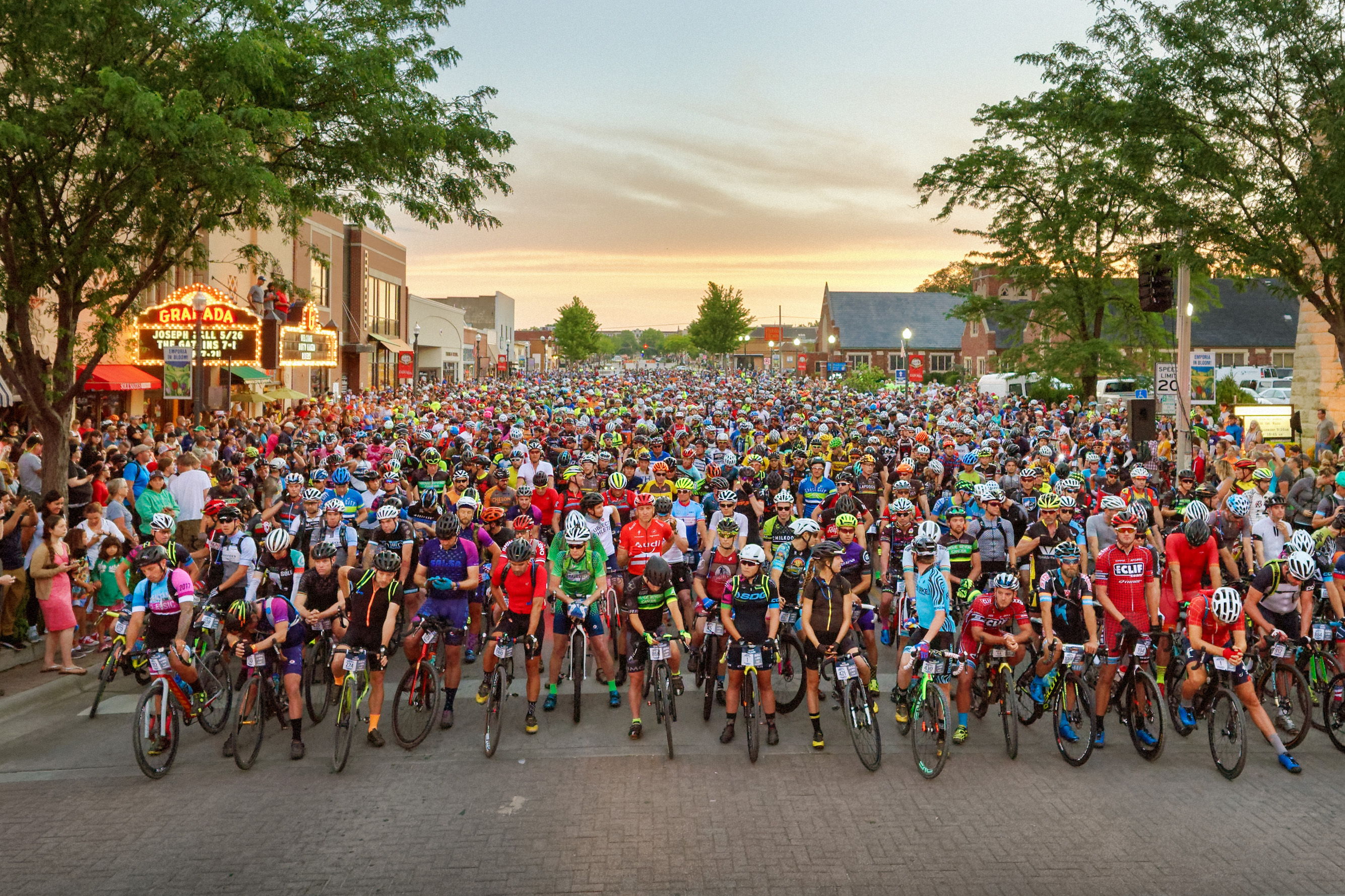 A vibrant group of cyclists in colorful gear gathers on the street, exuding excitement and camaraderie at a cycling event.