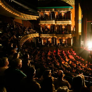 A lively concert in a grand theater captures an engaged audience, vibrant lighting, and a sense of community and celebration.
