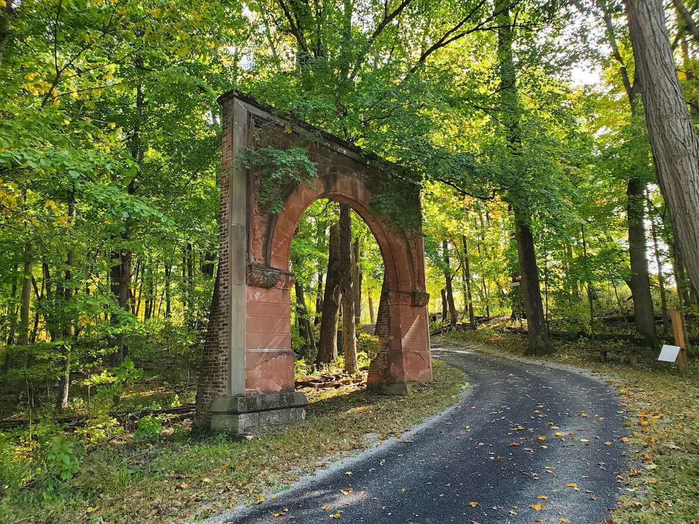 Rustic stone archway draped in greenery along a serene forest path, inviting tranquility and reflection in nature.