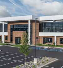 Modern commercial building with glass windows, brick and metal exteriors, surrounded by parking and landscaping, exuding professionalism.