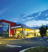 Modern community center with vibrant colors, well-lit entrance, surrounded by greenery under a twilight sky, evoking optimism.