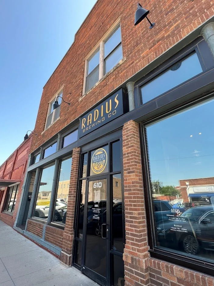Brick building with "RADIUS Brewing Co." storefront, large windows, urban setting, warm tones, inviting atmosphere.
