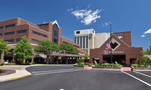 Modern hospital with brick facades, large windows, green landscaping, and a U.S. flag, conveying calmness and reassurance.