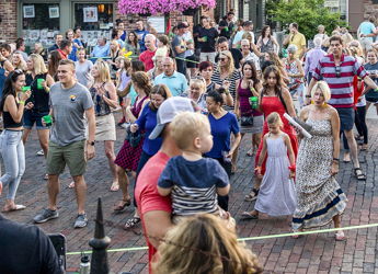 Outdoor gathering in a town square, with a diverse crowd celebrating joyfully, surrounded by flowers and American flags.