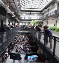 A lively, modern interior with multiple levels, large windows, greenery, and people engaged in conversation, fostering community.
