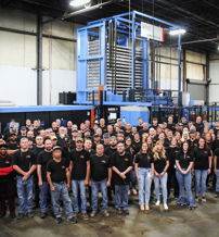 Group of smiling employees in black shirts at a factory, conveying teamwork, pride, and a sense of belonging.