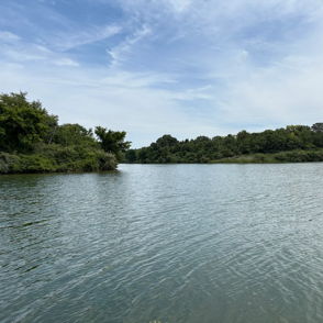 Serene lake surrounded by lush greenery; calm water reflects partly cloudy sky, evoking peace and tranquility.