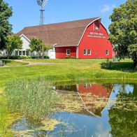 Charming rural scene with a red barn, white building, windmill, and serene pond under a blue sky, evoking tranquility.