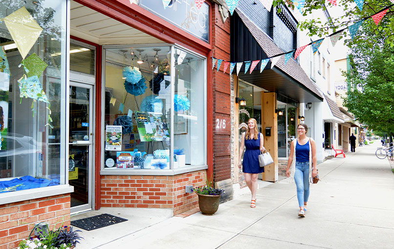 Lively street scene with women walking past colorful storefronts, conveying community, leisure, and a cheerful atmosphere.