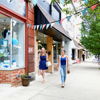 Lively street scene with women walking past colorful storefronts, conveying community, leisure, and a cheerful atmosphere.
