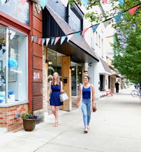 Lively street scene with women walking past colorful storefronts, conveying community, leisure, and a cheerful atmosphere.