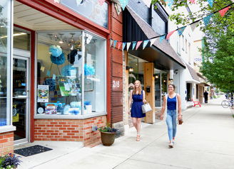 Lively street scene with women walking past colorful storefronts, conveying community, leisure, and a cheerful atmosphere.