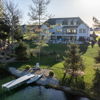Serene lakeside scene with a modern house, lush greenery, tranquil water, and a dock, evoking peace and harmony with nature.