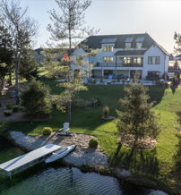 Serene lakeside scene with a modern house, lush greenery, tranquil water, and a dock, evoking peace and harmony with nature.