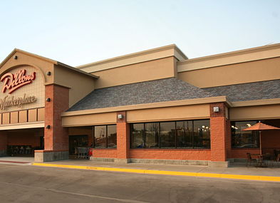 Exterior of a large commercial building, inviting with warm tones, outdoor seating, and large windows, suggesting community and relaxation.