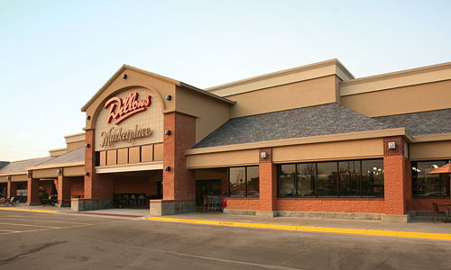 Exterior of a large commercial building, inviting with warm tones, outdoor seating, and large windows, suggesting community and relaxation.