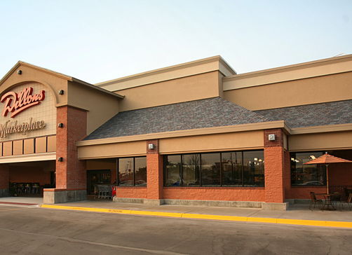 Exterior of a large commercial building, inviting with warm tones, outdoor seating, and large windows, suggesting community and relaxation.