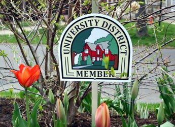 "Sign saying 'University District Member' amidst colorful tulips, evoking community pride and connection to nature."