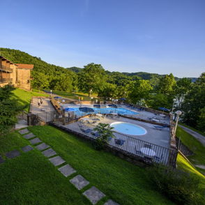 Serene resort scene with a pool, lush greenery, and hills, evoking relaxation and tranquility under a clear blue sky.