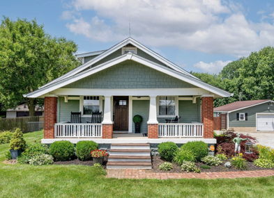 Charming light green house with white trim, inviting porch, and landscaped yard, evoking warmth and tranquility in suburbia.