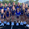 Cheerleaders in blue and black uniforms smile together on a track field, exuding joy, camaraderie, and team spirit.