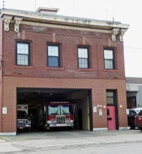 Brick fire station with a garage, classic design, nearby vehicles; evokes safety, nostalgia, stability, and community spirit.