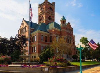 Historic courthouse with clock tower, ornate brickwork, green accents, and vibrant landscaping, evoking community and nostalgia.