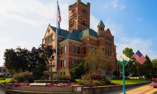 Historic courthouse with clock tower, ornate brickwork, green accents, and vibrant landscaping, evoking community and nostalgia.