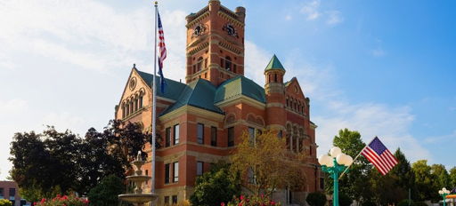 Historic courthouse with clock tower, ornate brickwork, green accents, and vibrant landscaping, evoking community and nostalgia.