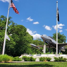 Military aircraft on a pedestal, surrounded by flags, set against a blue sky, symbolizing patriotism and honor.