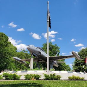 Military aircraft on a pedestal, surrounded by flags, set against a blue sky, symbolizing patriotism and honor.