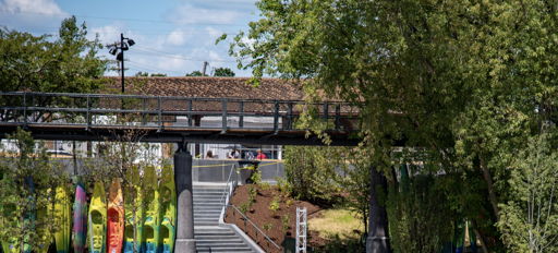 Colorful kayaks line a dock by a serene water body, where people enjoy a sunny day in a vibrant, green setting.