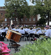 Outdoor band performance in a vibrant park, with colorful flowers and an audience, evoking community joy and togetherness.