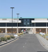 A modern glass building with a landscaped approach, paved road, and clear blue sky evokes professionalism and tranquility.
