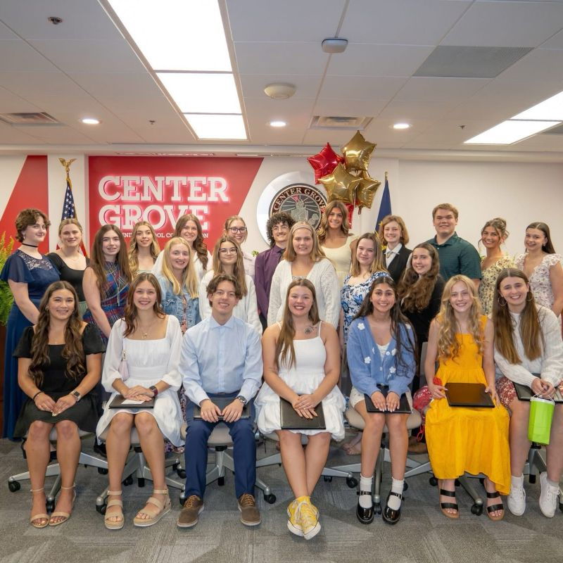 A joyful gathering of diverse young individuals in festive attire, celebrating achievements at an event with "CENTER GROVE" signage.