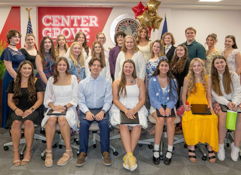 A joyful gathering of diverse young individuals in festive attire, celebrating achievements at an event with "CENTER GROVE" signage.