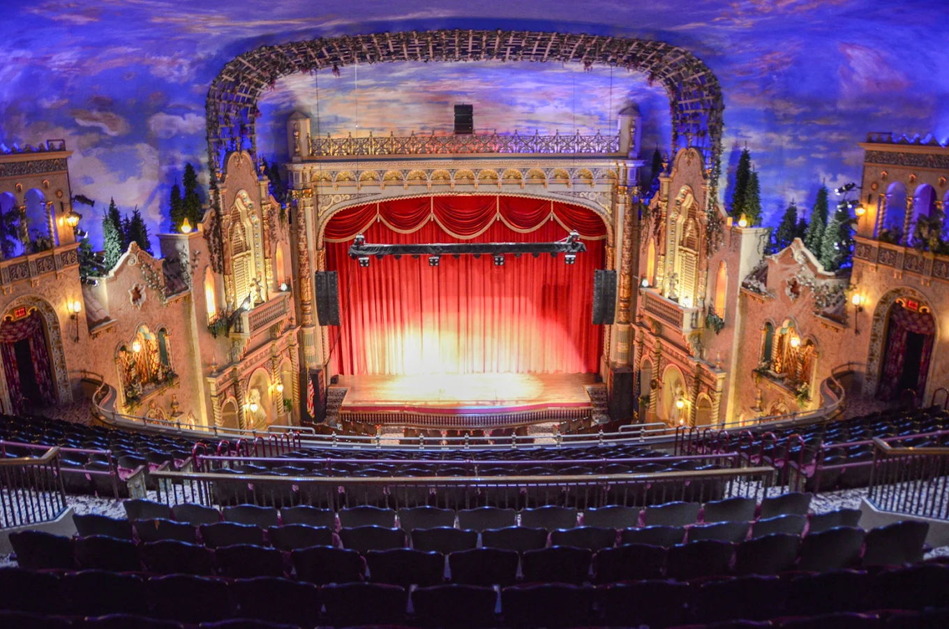 Grand theater interior with ornate decor, a vibrant stage, and deep red curtains, evoking anticipation for a live performance.