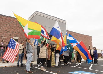 Diverse group outdoors, holding flags from various countries, conveys unity, pride, and celebration in a vibrant atmosphere.